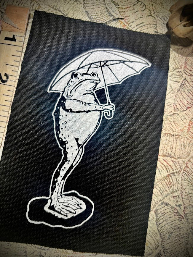 Sad frog holding an umbrella in the rain patch.